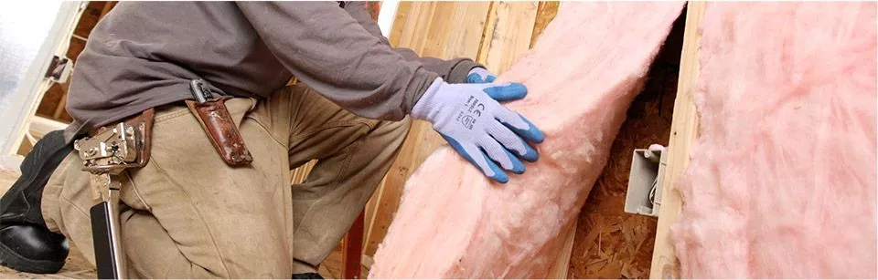 Technician installing pink fiberglass batt insulation into the wall of a house