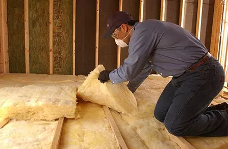 Attic installer adding yellow batt insulation to the floor of the attic.