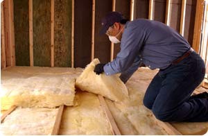 Technician kneeling while installing fiberglass insulation in an attic floor.